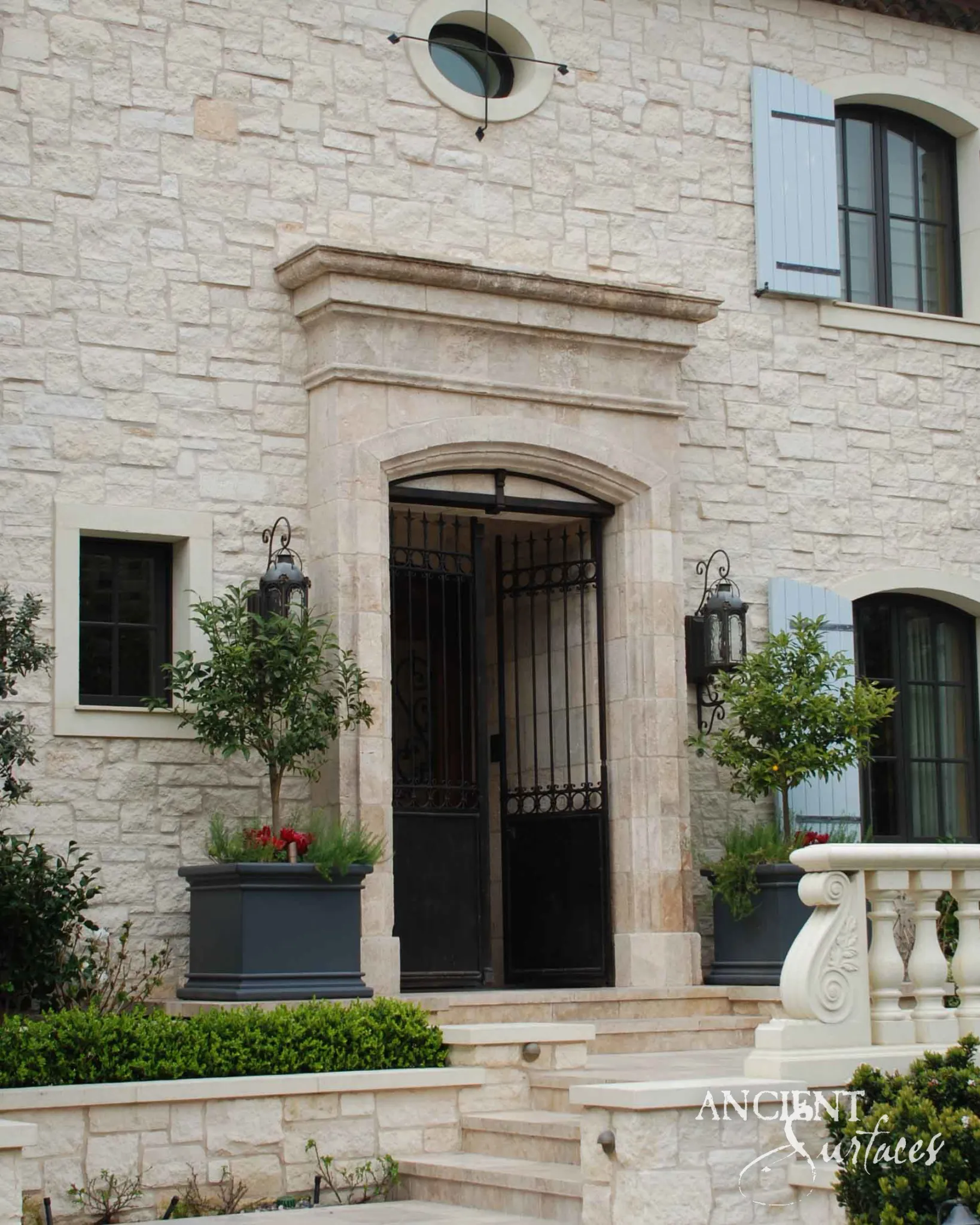 Cream limestone door surround with a moulded cornice over a round-arched iron gate